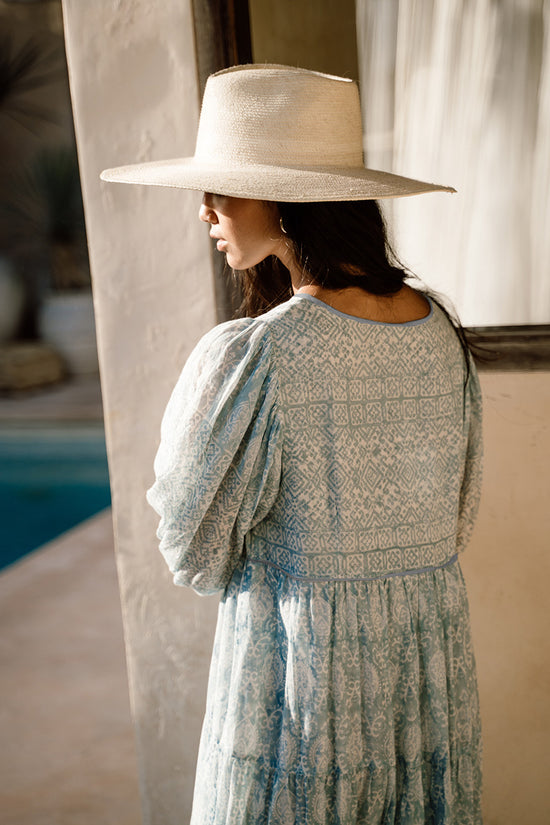 Jasmine Maxi Dress Sea Mist — back view with straw hat, riad archway with pool beyond, showing block print upper panel and tiered skirt, hand block print sea mist cotton, artisan Jaipur boho maxi | Daughters of India