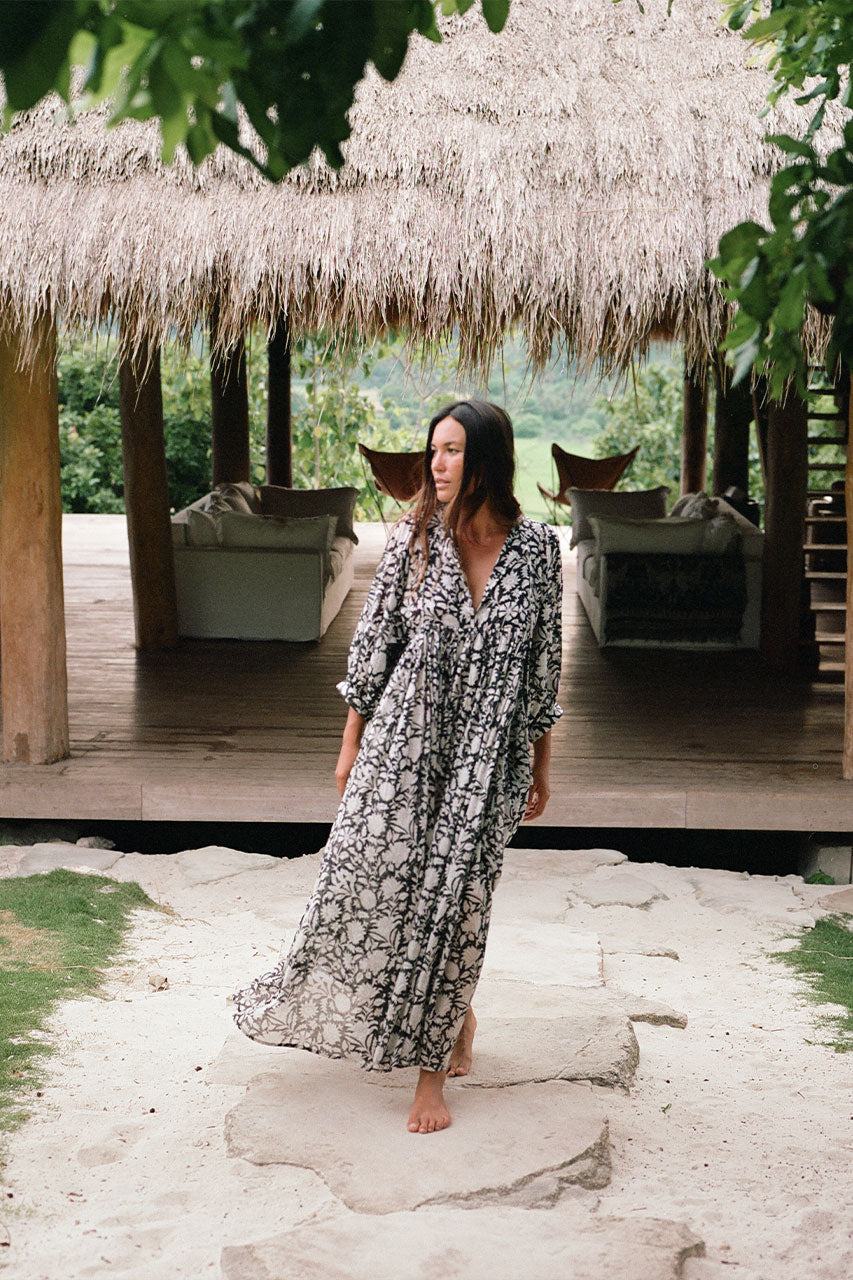 Daughters of India Kyra Maxi Dress in Pepper — full length walking toward thatched hut, flowing hand screen print skirt