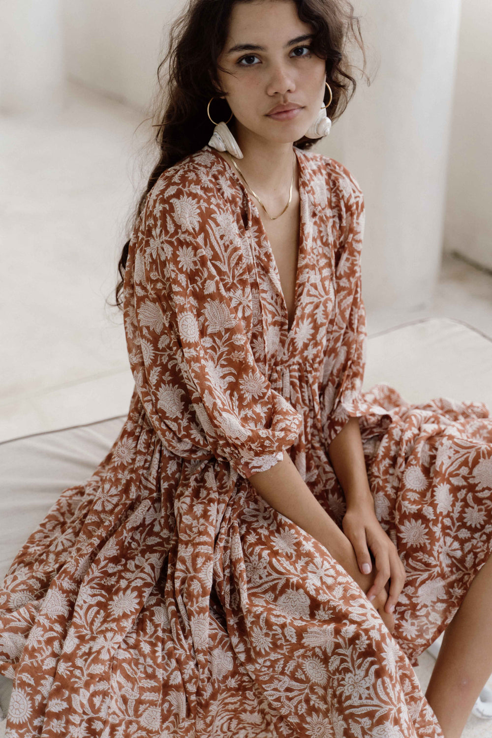 Daughters of India Kyra Midi Dress in Caramel — seated on white linen, V-neckline and neckline tie, floral print