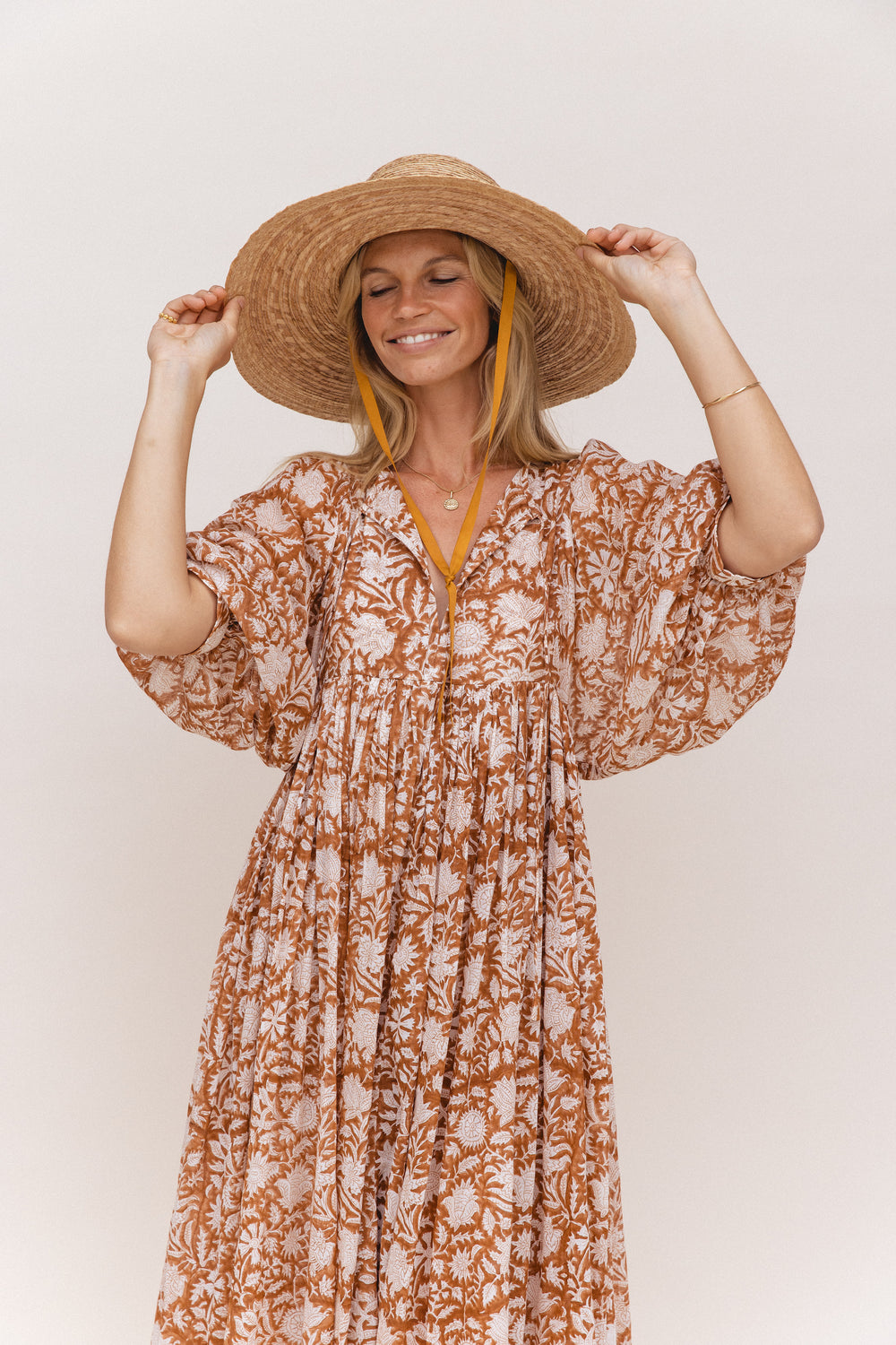 Daughters of India Kyra Midi Dress in Caramel — studio upper body smiling with straw hat, billowed sleeves, gathered waist