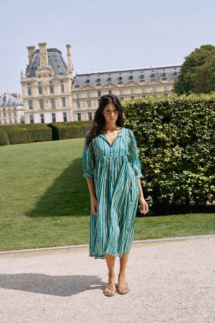 Woman standing in front of a historic European building and formal gardens wearing the Daughters of India Kyra Midi Dress in Spearmint