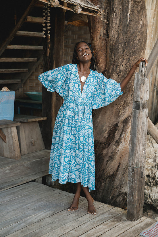 Daughters of India Kyra Midi Dress in Ocean Blue — smiling on wooden deck of tropical treehouse, billowed sleeves