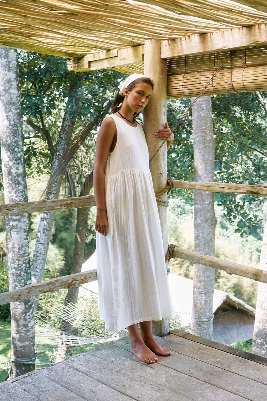 Nadi Dress White — full length front view on tropical balcony, white double gauze cotton midi dress with flowing gathered skirt, bamboo railing and greenery | Daughters of India
