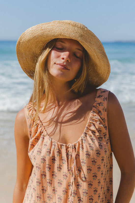 Sundress Midi Peach — model seated outdoor, relaxed pose showing gathered skirt fall, peach floral block print cotton dress, sleeveless sundress, artisan made Jaipur India | Daughters of India